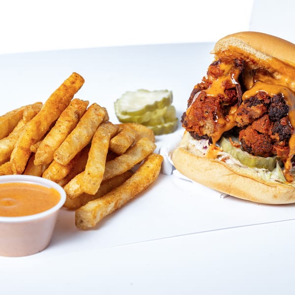 Hot Birds fried chicken sandwich with sauce, pickles, and a side of fries with dipping sauce.