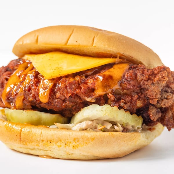 Hot Birds fried chicken sandwich with melted cheese, sauce, pickles, and coleslaw on a bun.