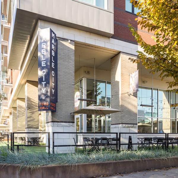 Exterior of Marble City Food Hall with outdoor seating, umbrellas, and a prominent sign.