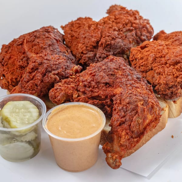 Hot Birds fried chicken pieces with pickles and sauce on white bread.