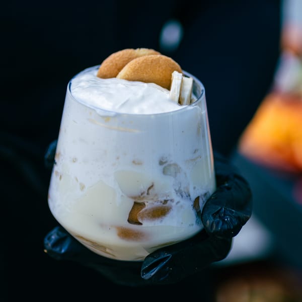 A Hot Birds banana pudding dessert in a glass, topped with whipped cream and vanilla wafers.