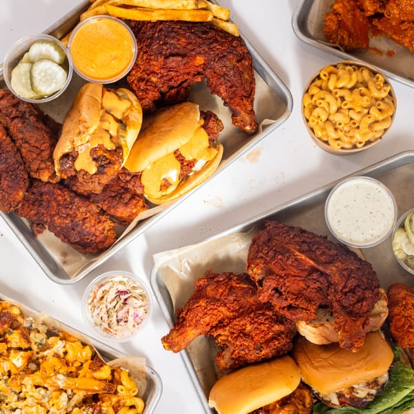 Overhead view of Hot Birds fried chicken, sandwiches, fries, mac and cheese, and coleslaw on metal trays.