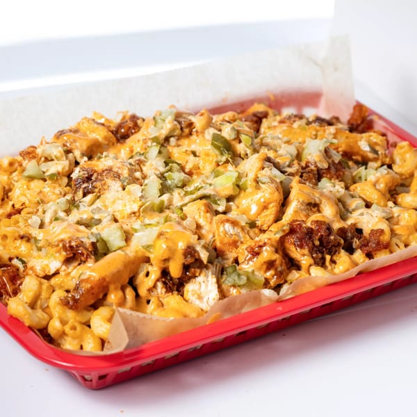 Hot Birds' fried chicken mac and cheese, topped with sauce and diced pickles, in a red basket.